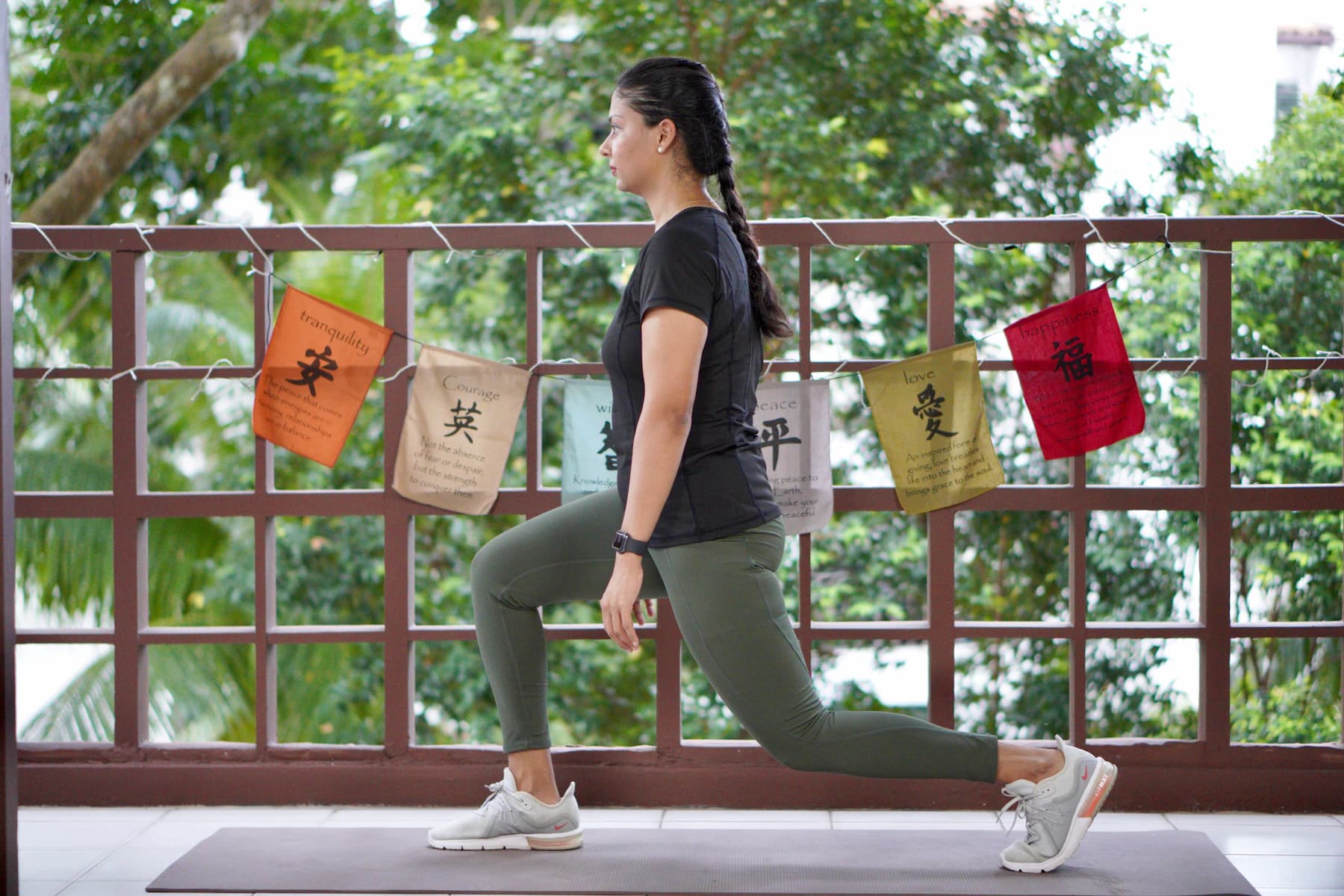 A woman does a lunge on an exercise mat on a balcony at home